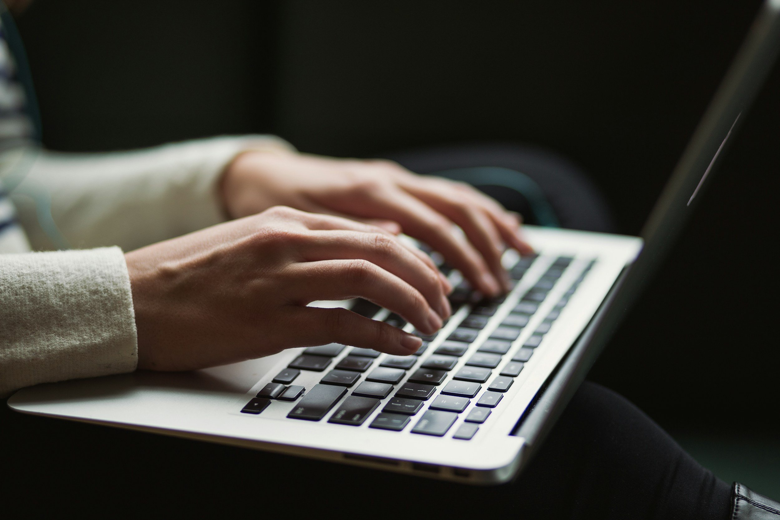 Person typing on a laptop keyboard with a dark background.