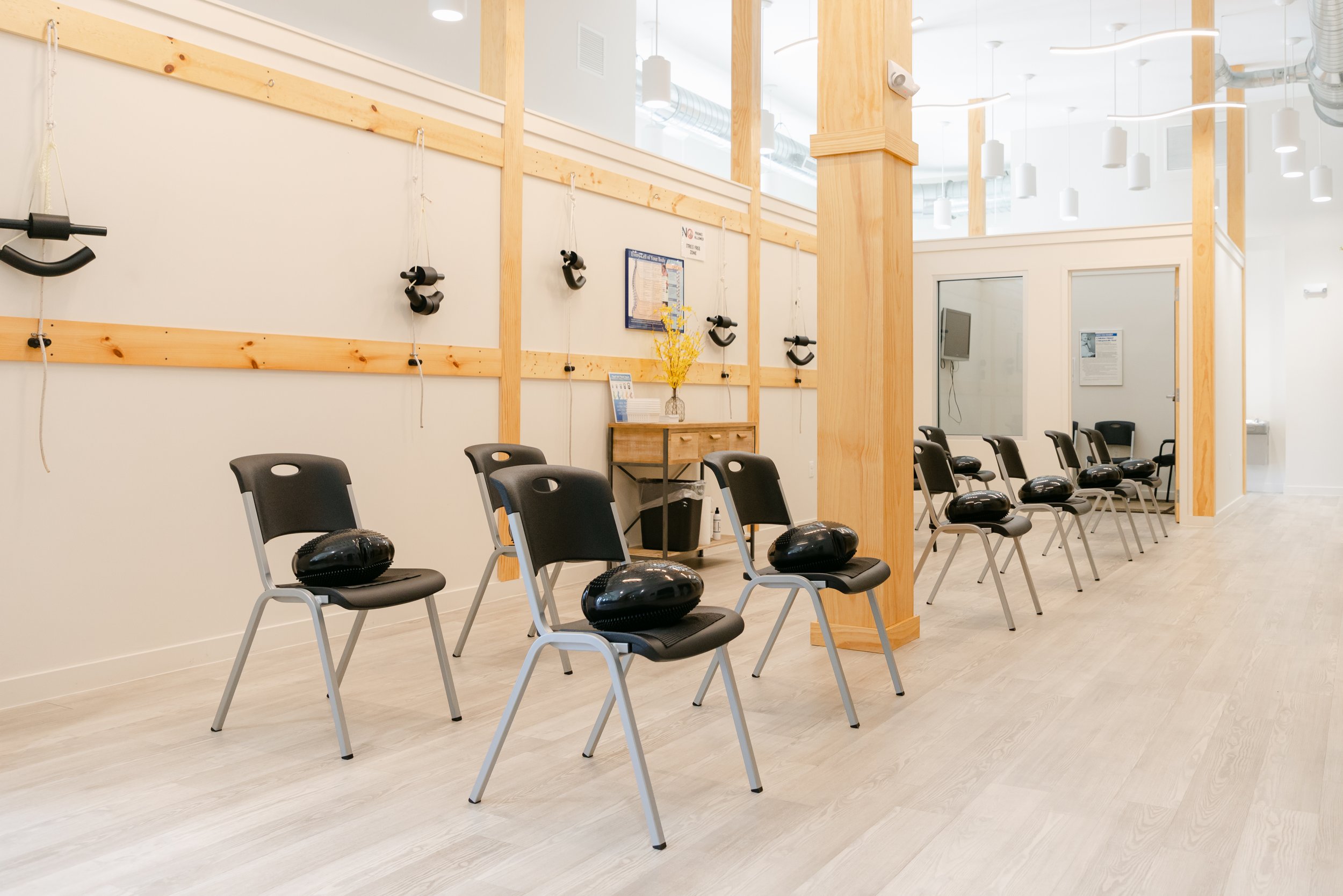 A room with chairs and black pedometers placed on them, set up for a fitness or health class, with a wooden divider wall and light-colored flooring.