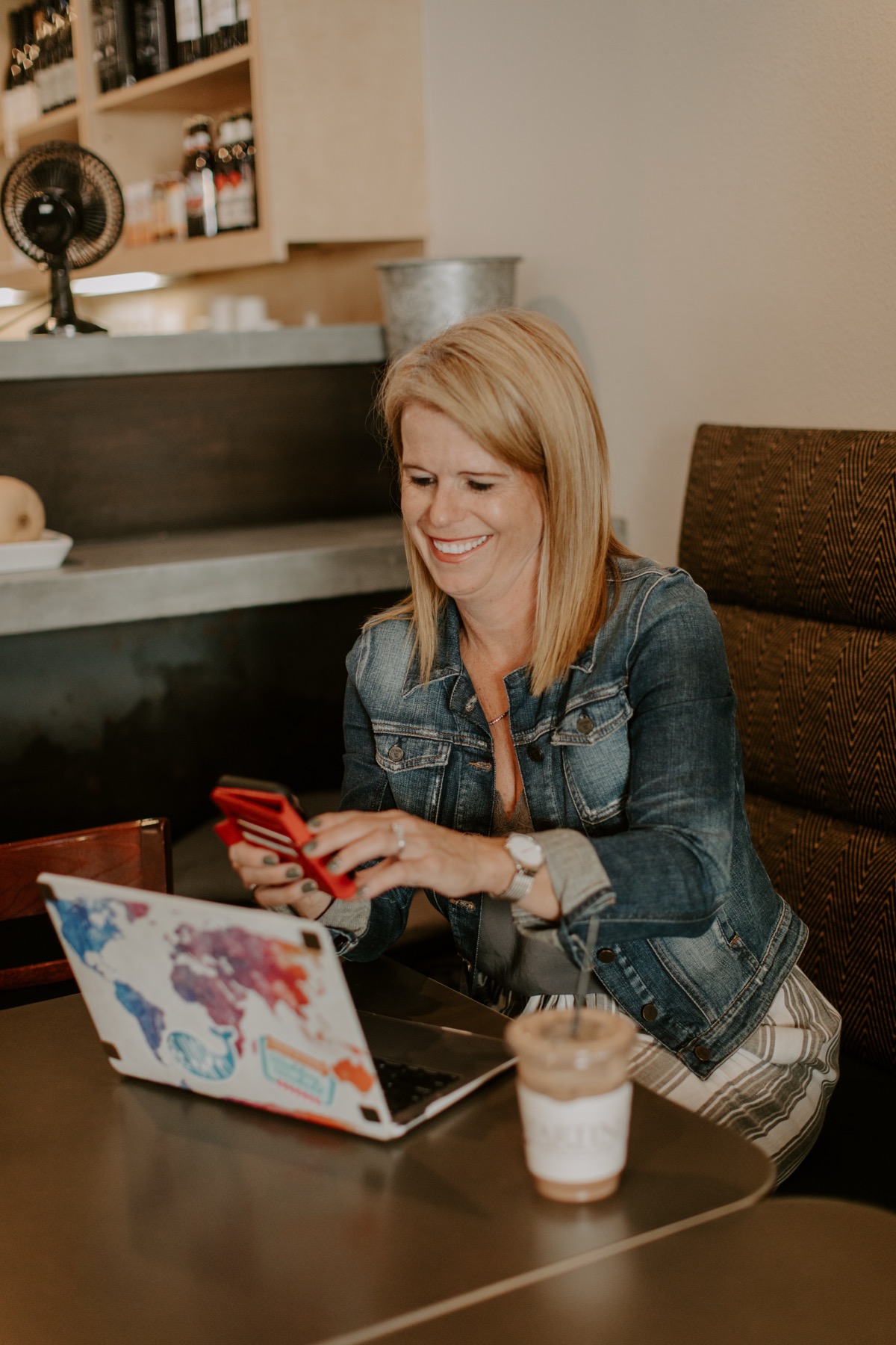 Laura Nelson smiling at her phone with her laptop open at a cafe
