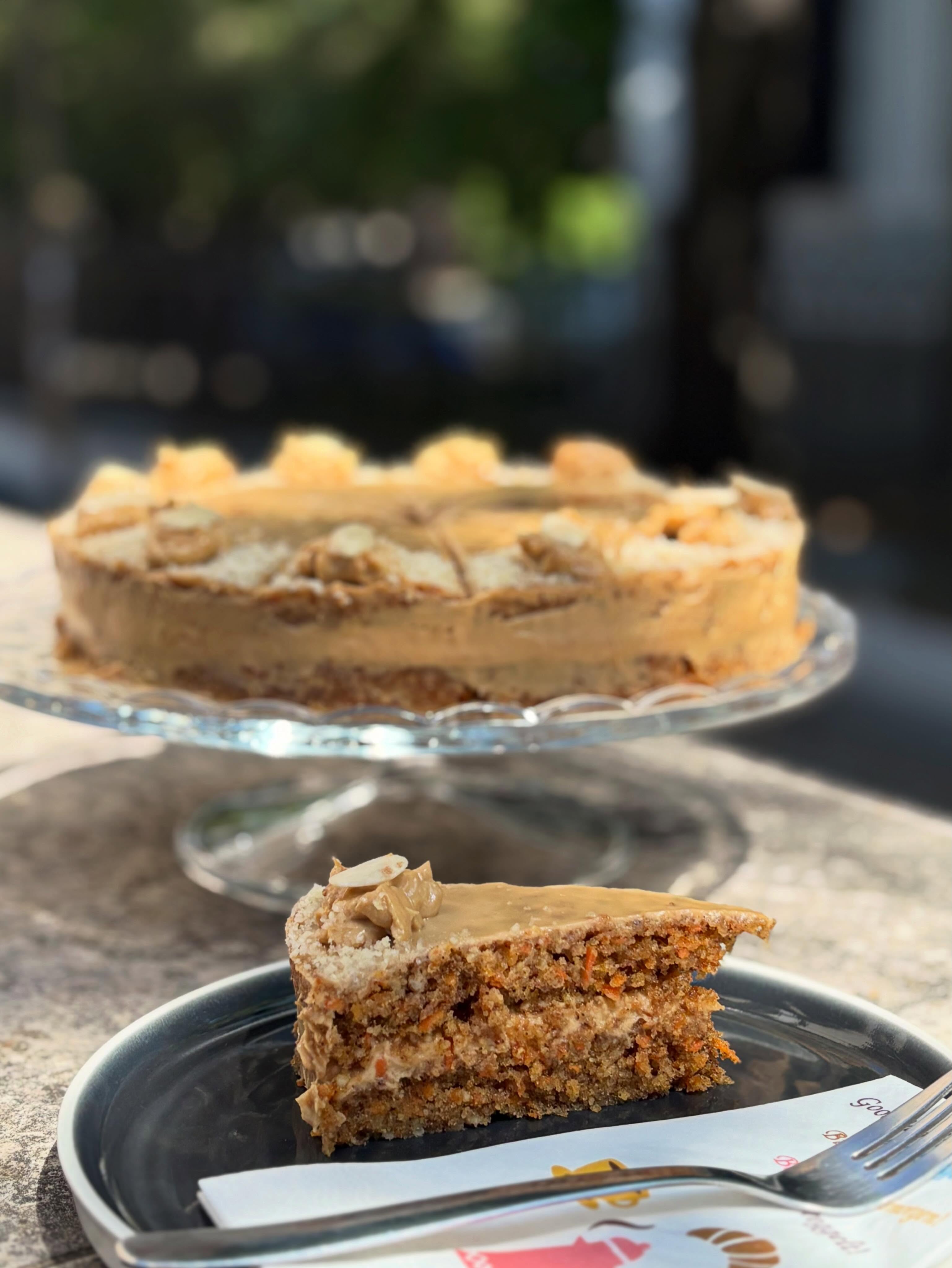 Tortaszelet tányéron, mögötte torta üvegtálon