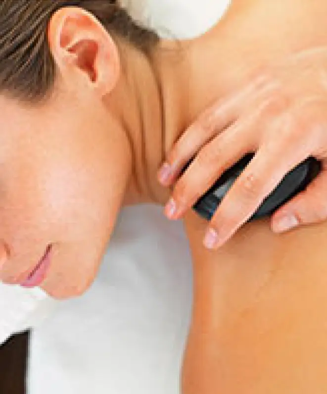 Close-up of a person receiving a hot stone massage on their shoulder and upper back area.