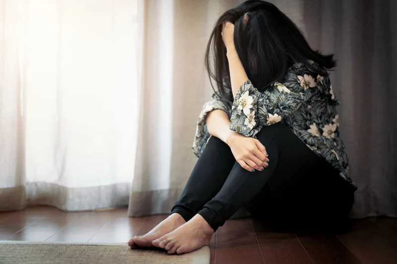 Of a depressed woman sitting on the floor, bent down with her face. In her hands- Awaiting treatment for depression.
