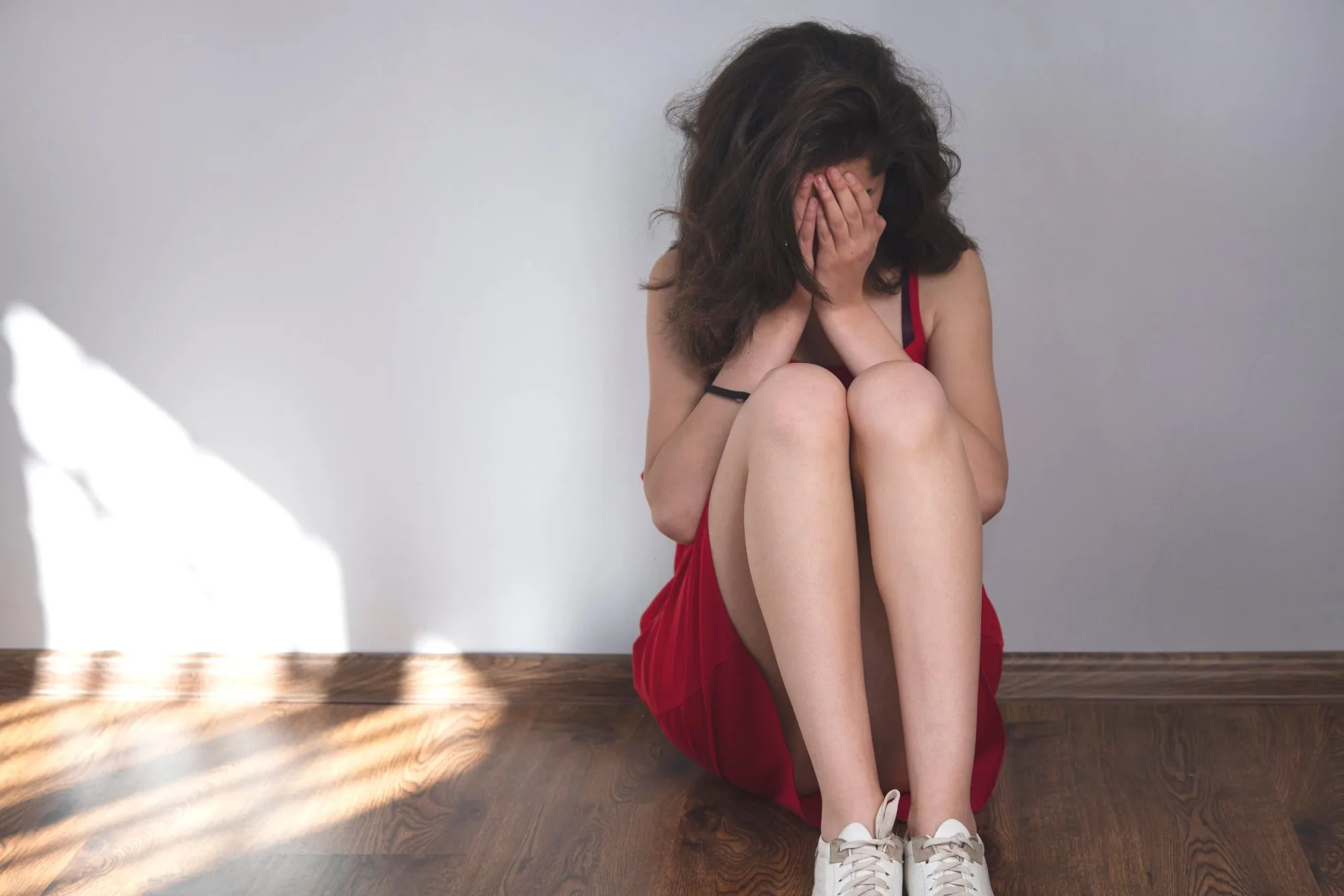 Woman sitting on floor with hands covering face, representing the emotional weight of major depressive disorder