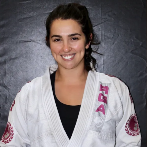 Coach Lauren, a dedicated purple belt Brazilian jiu jitsu practitioner with 6 years of experience, proudly stands as the head coach of the women's classes at Renzo Gracie Weston Academy, wearing her gi and holding a clipboard with class plans, inspiring the next generation of female martial artists.