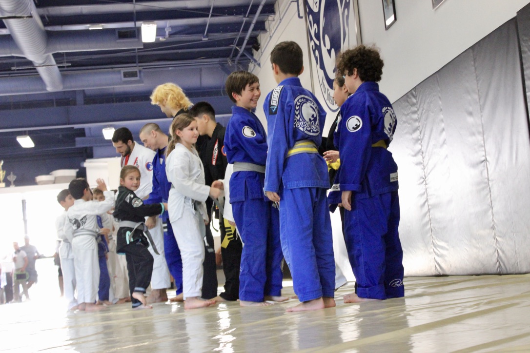 Diverse group of young children in jiu-jitsu uniforms demonstrating respect and discipline by bowing after a successful training session on the dojo mats, embodying the values of humility and cooperation in martial arts.