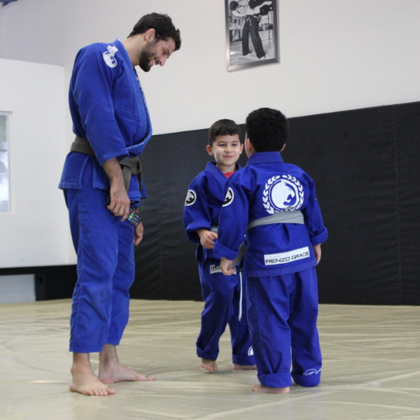 Two enthusiastic children attentively learning Brazilian Jiu-Jitsu techniques from Head Coach Adrian Alsina at Renzo Gracie Academy of Weston, known for empowering young minds through discipline and physical activity.