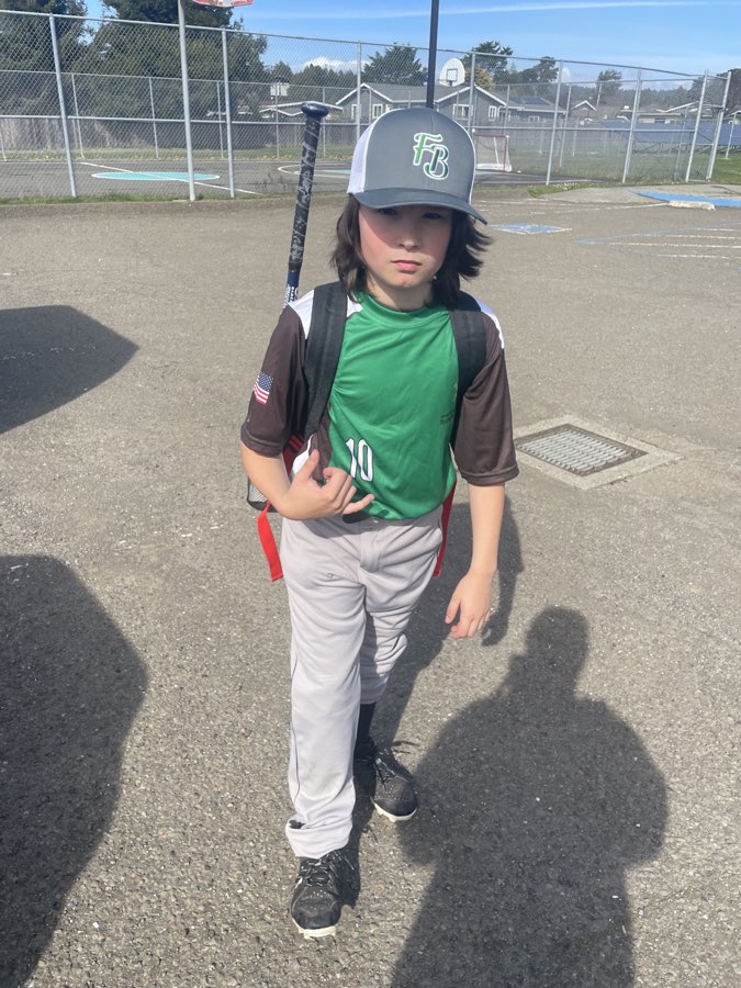 Bodhi walking with his bat bag in his green baseball jersey.
