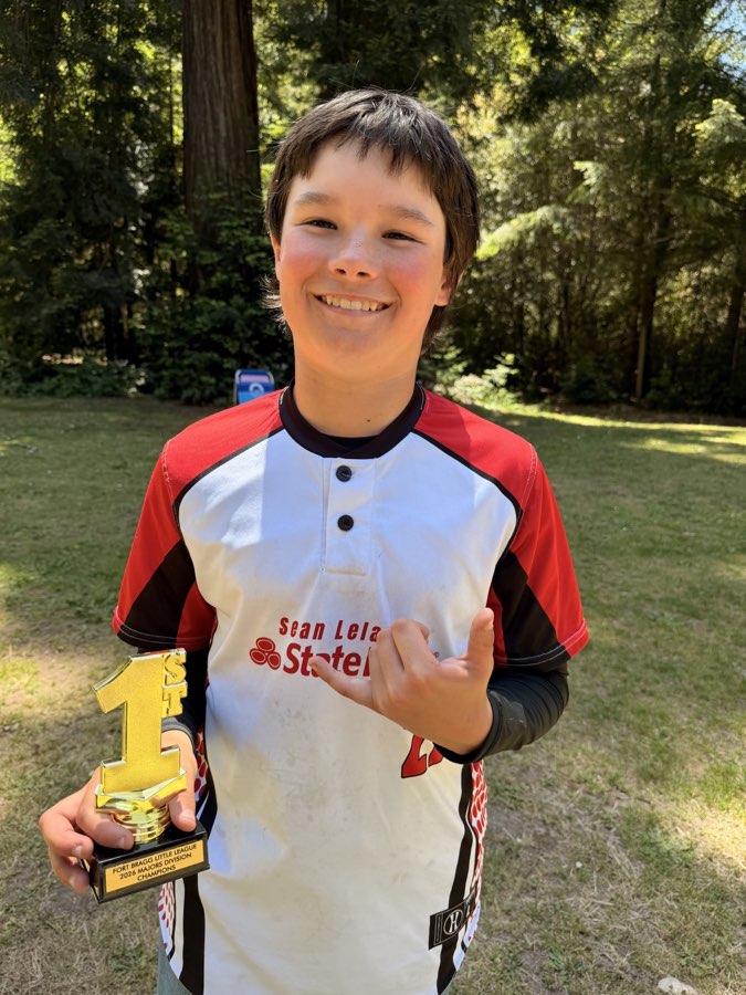Bodhi smiling in his baseball uniform while holding a trophy.