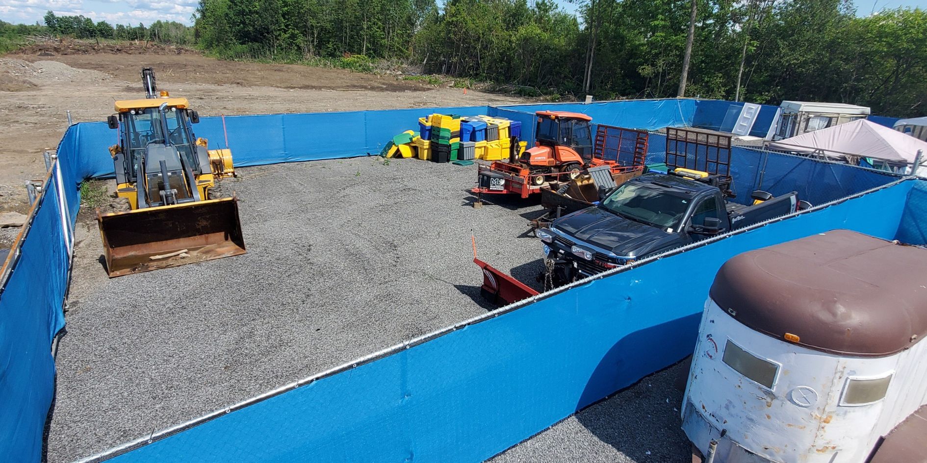 Fenced yard at Longyards Ottawa holding a loader, a pickup truck and trailers