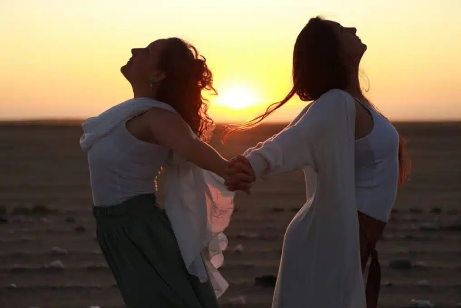 Women holding hands in a circle at sunset