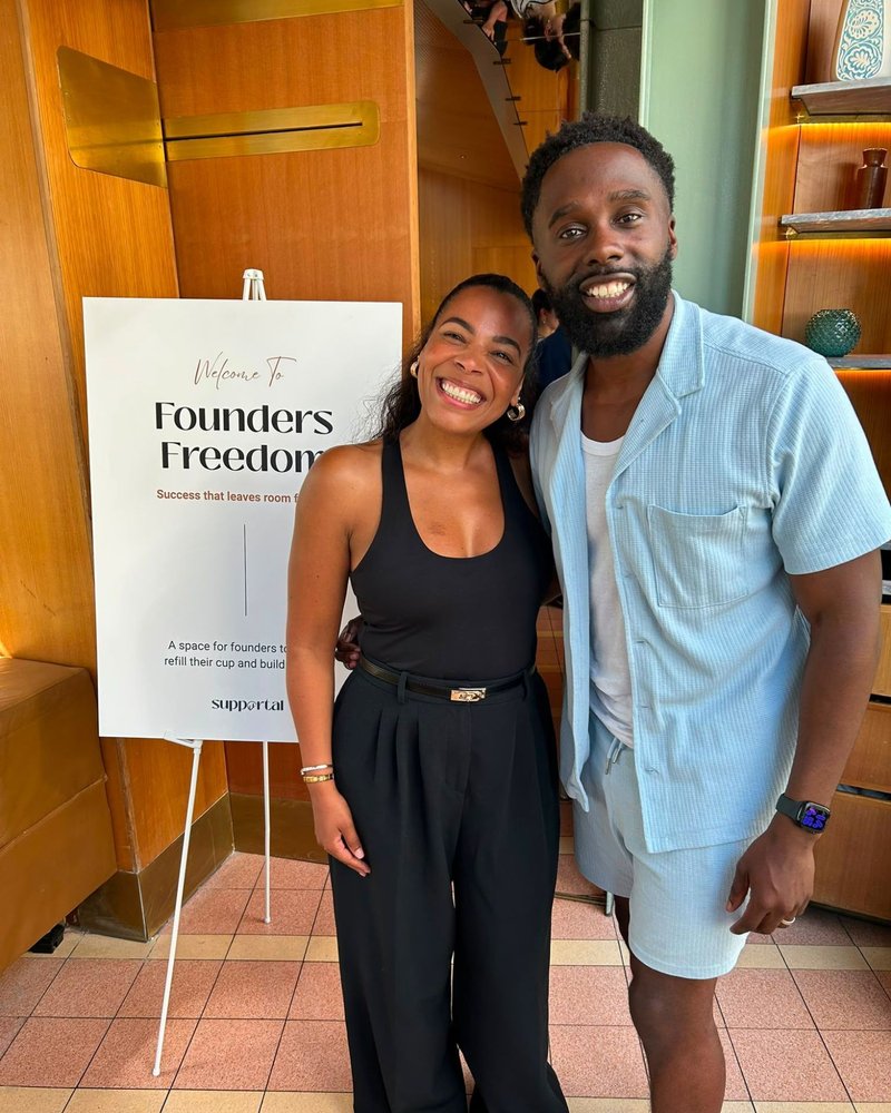 Two hosts smiling beside the Welcome to Founders Freedom sign