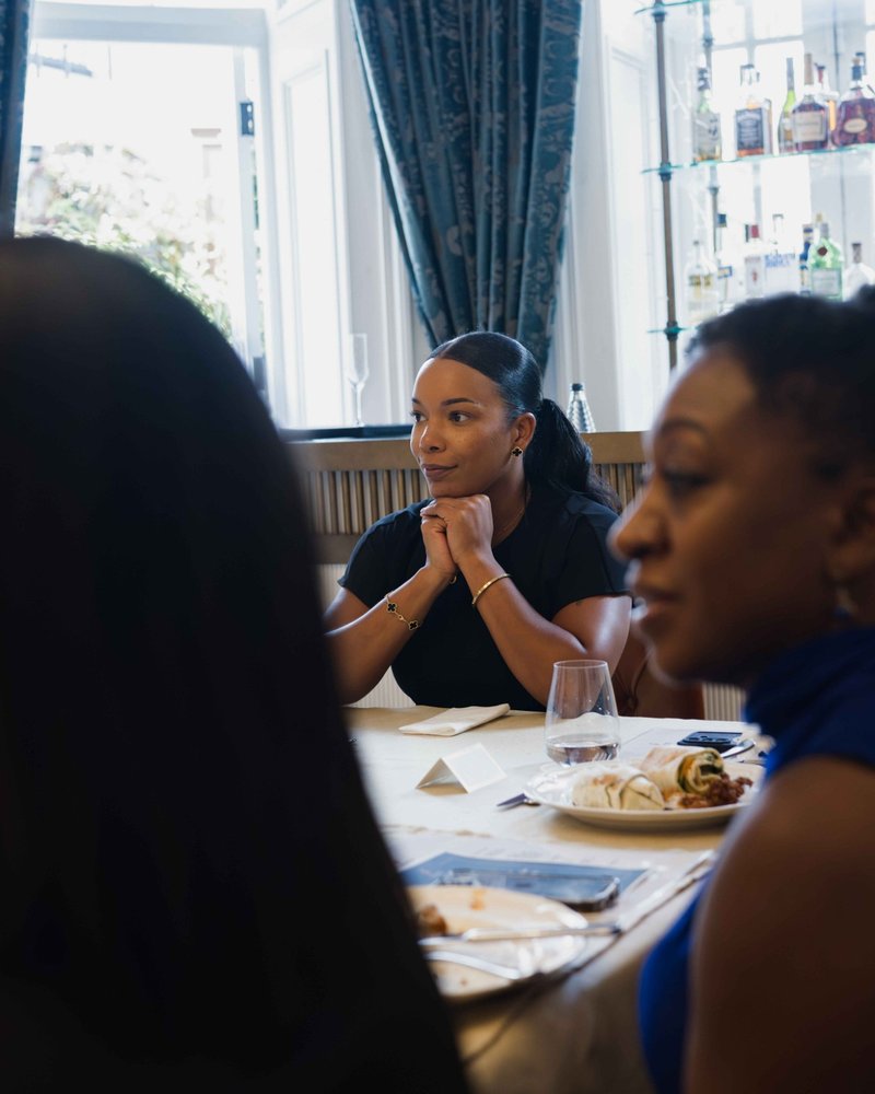 A founder listening, chin on her hands, at a table by the window