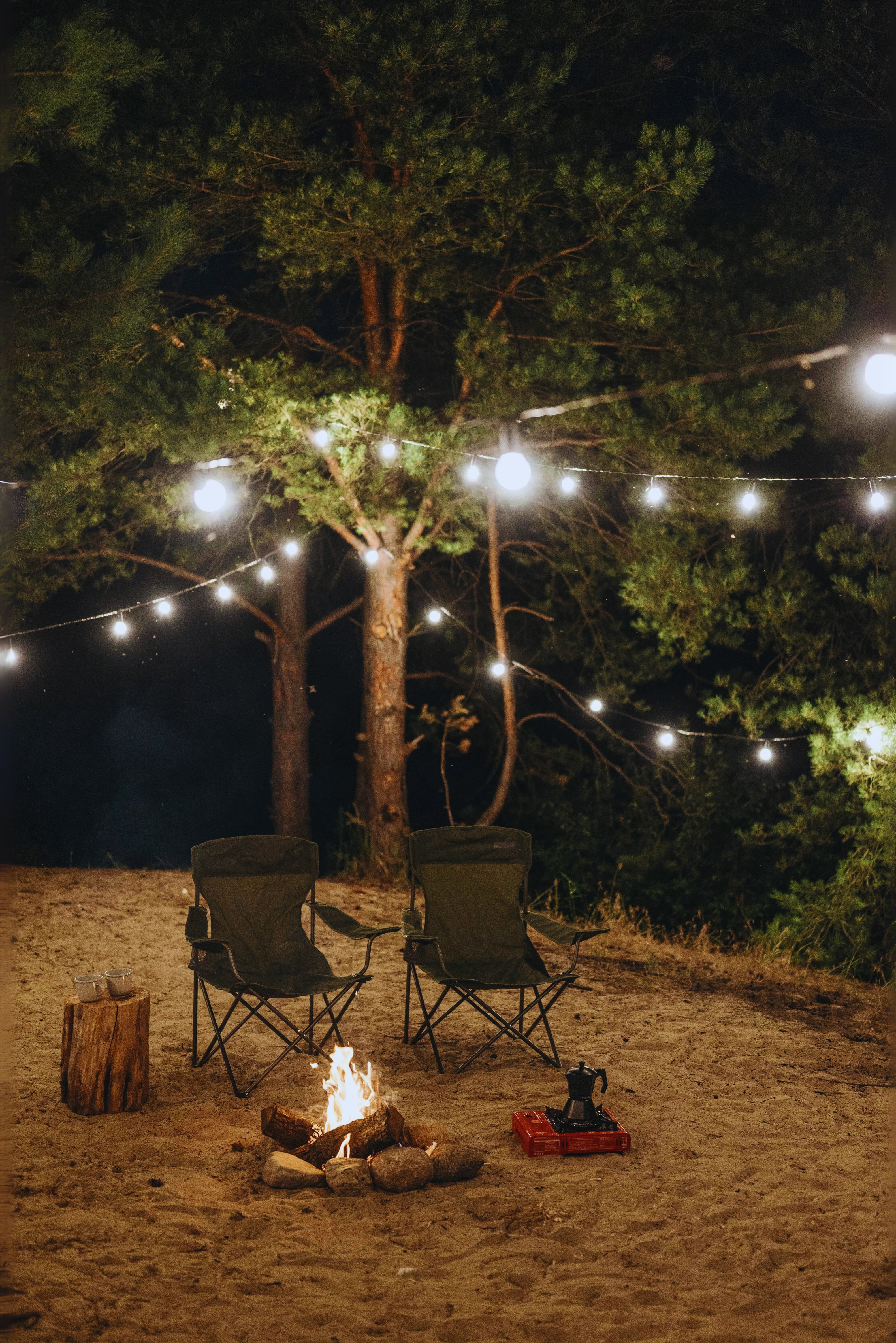 Two camping chairs beside a glowing campfire under string lights at West Canada Creek Campground in Poland, NY