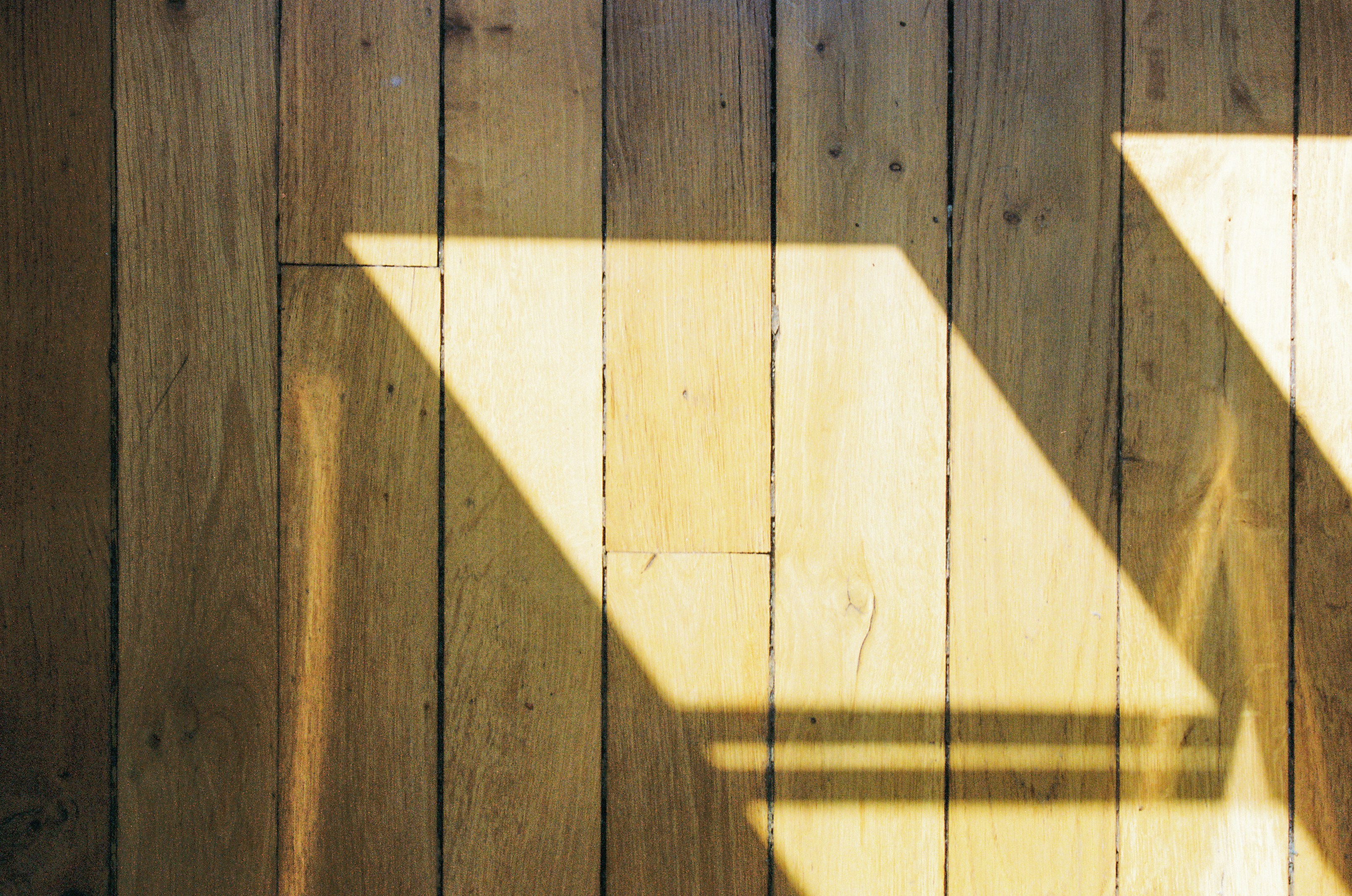 Afternoon window light casting geometric shadows across oak floorboards