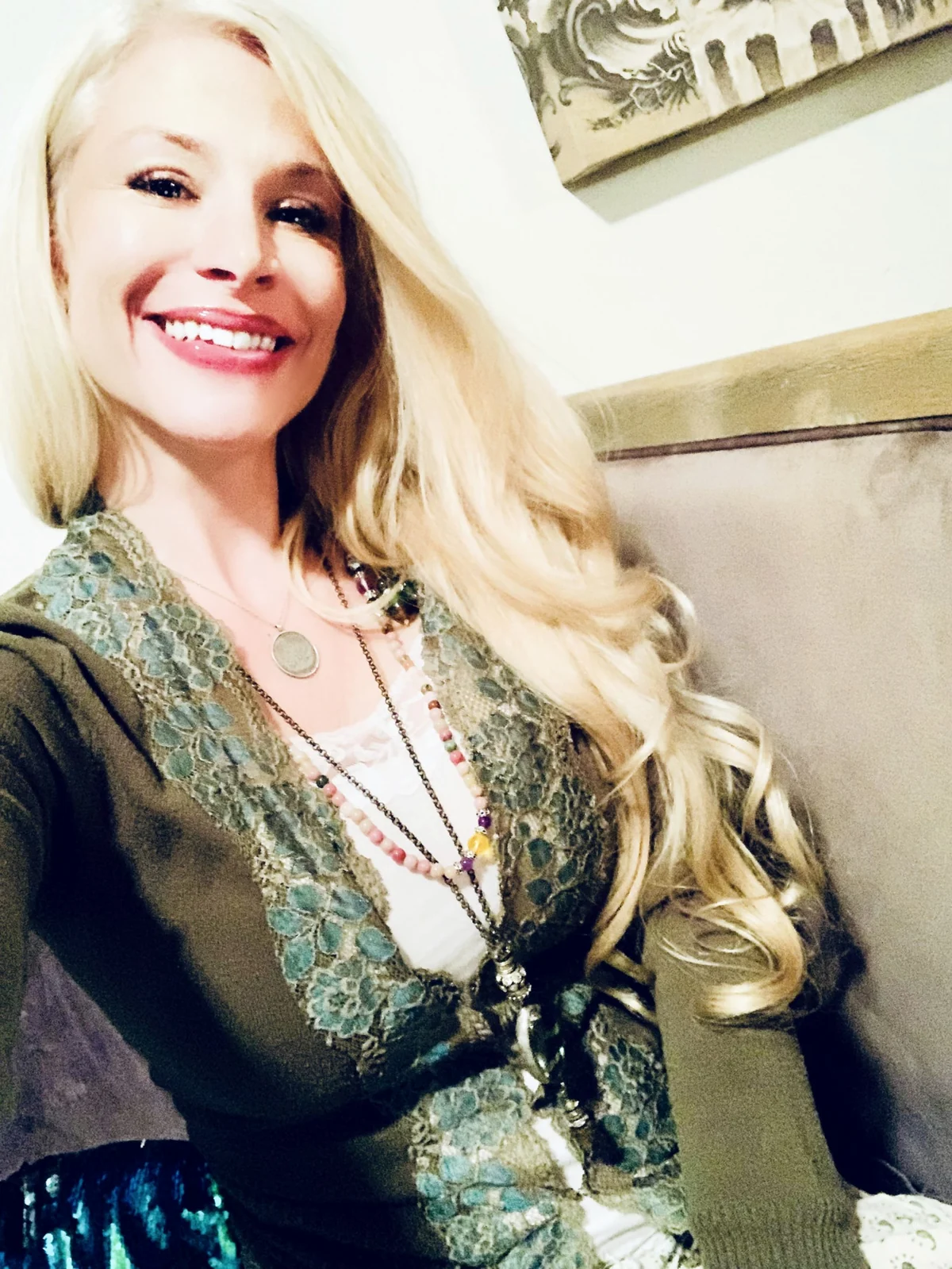 Molly Rose Holmes smiling in an olive lace cardigan with layered beaded necklaces