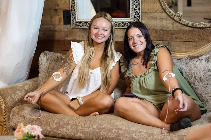 Two clients smiling on a couch while receiving mobile IV therapy at home