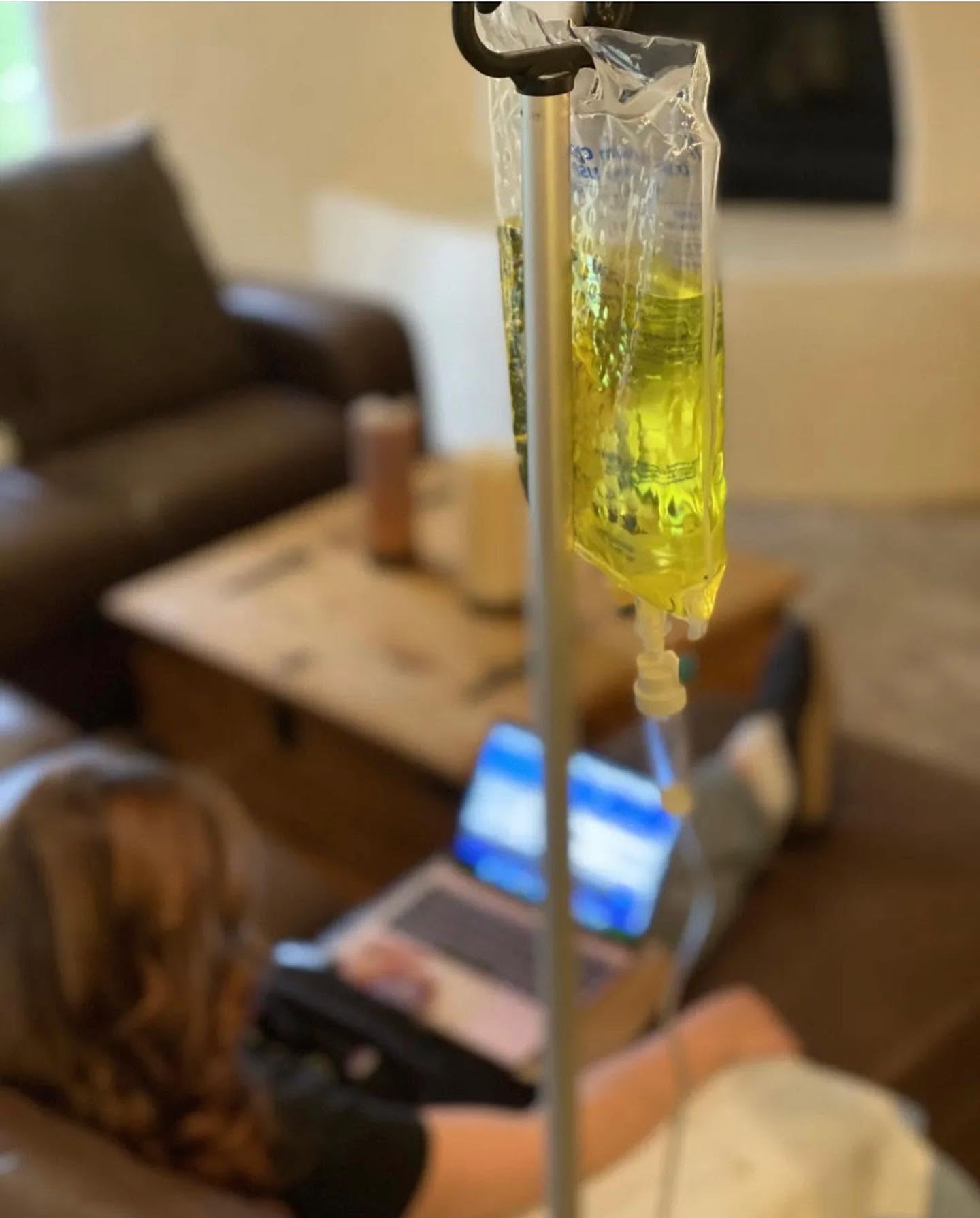 IV bag hanging while a client works on a laptop during their infusion