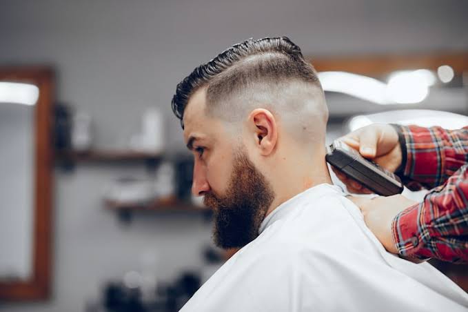 Barber carefully completing a detailed men's fade and beard trim