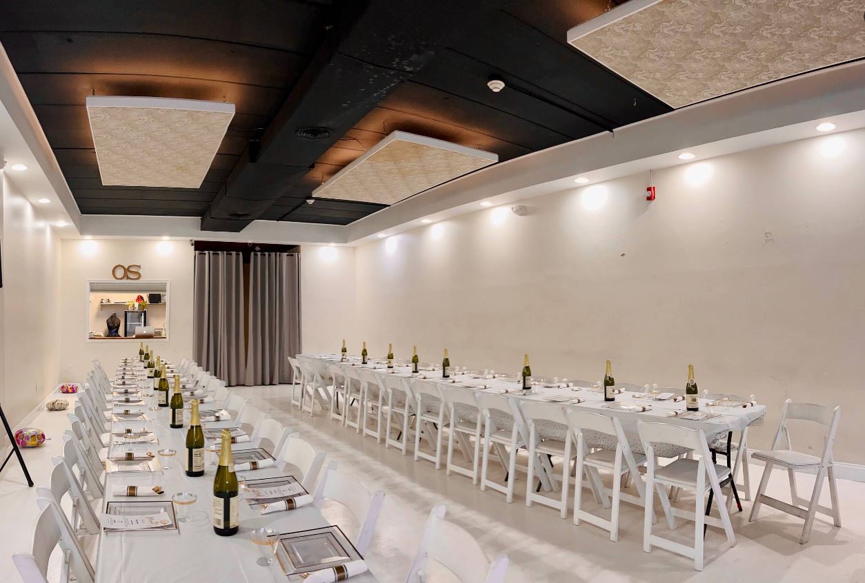 Open Space gallery arranged with long dining tables and white chairs beneath geometric ceiling lighting