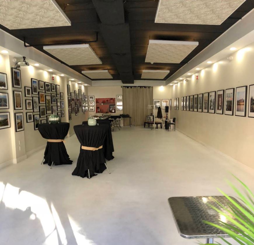 Open Space gallery with artwork, a polished white floor, and cocktail tables