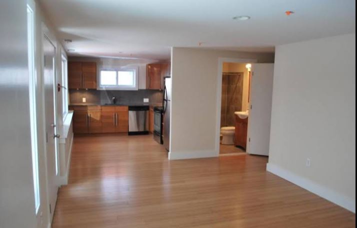 Unfurnished apartment living area with wood flooring and adjoining kitchen
