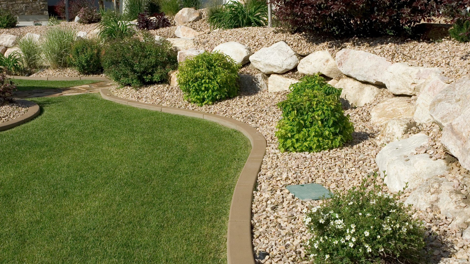 Lawn edge bordered by boulders and green shrubs — a healthy landscape by Oak and Stone Landscaping, Sacramento