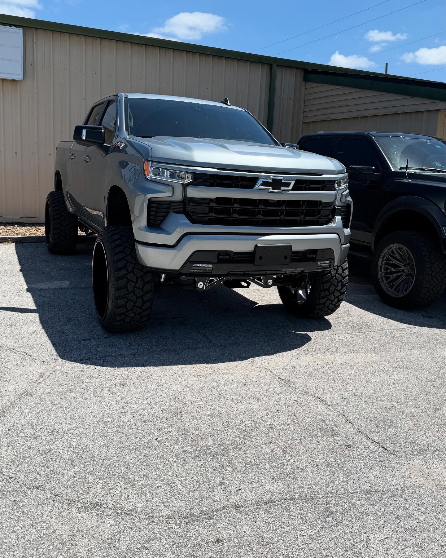 Lifted gray Chevy Silverado 1500 on black wheels outside the Top Trucks shop