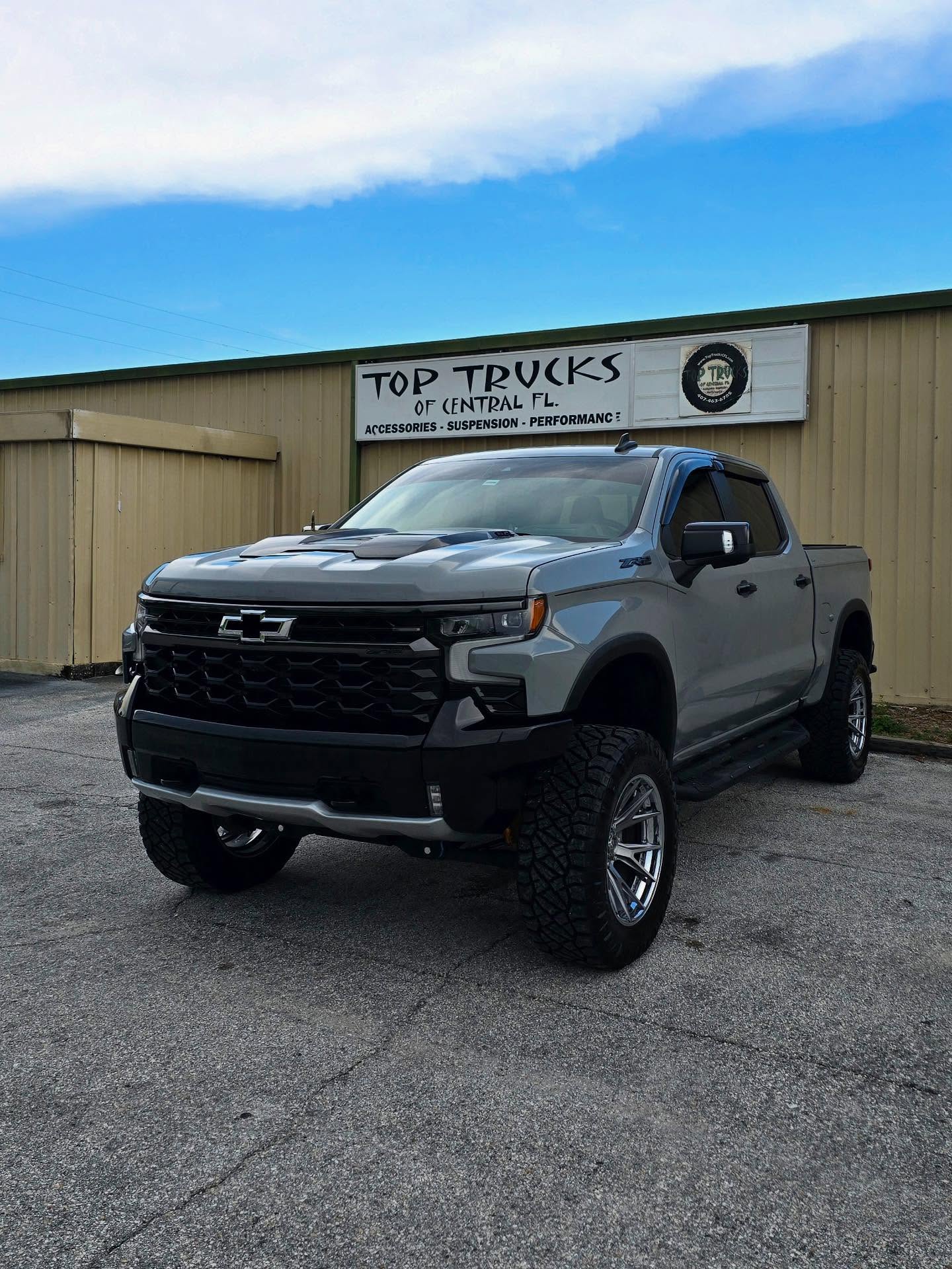Lifted gray Chevy Silverado outside the Top Trucks shop