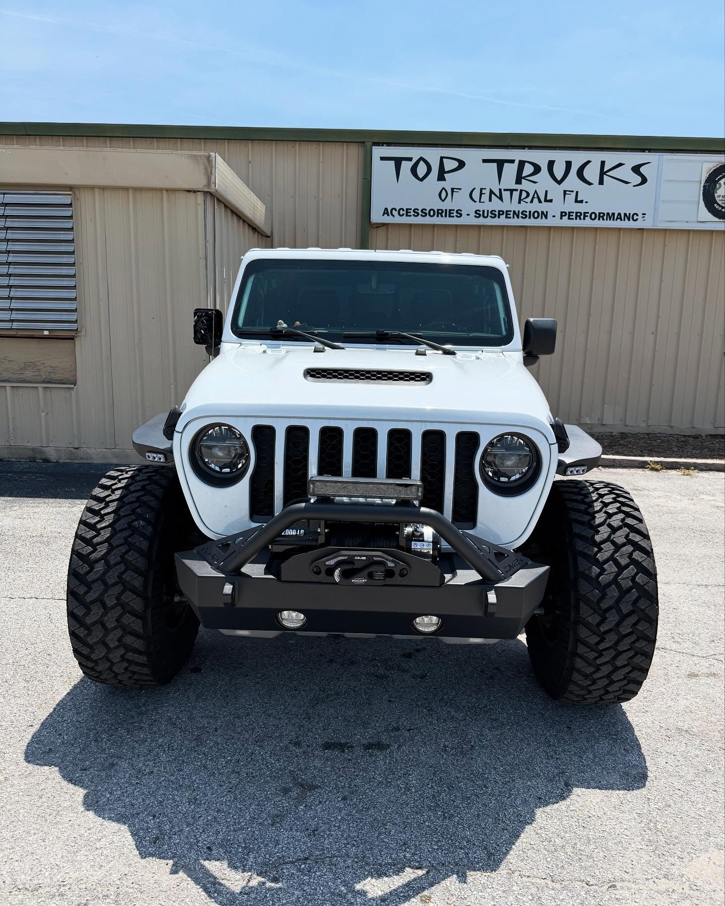White Jeep Wrangler with an aftermarket front bumper outside the Top Trucks shop