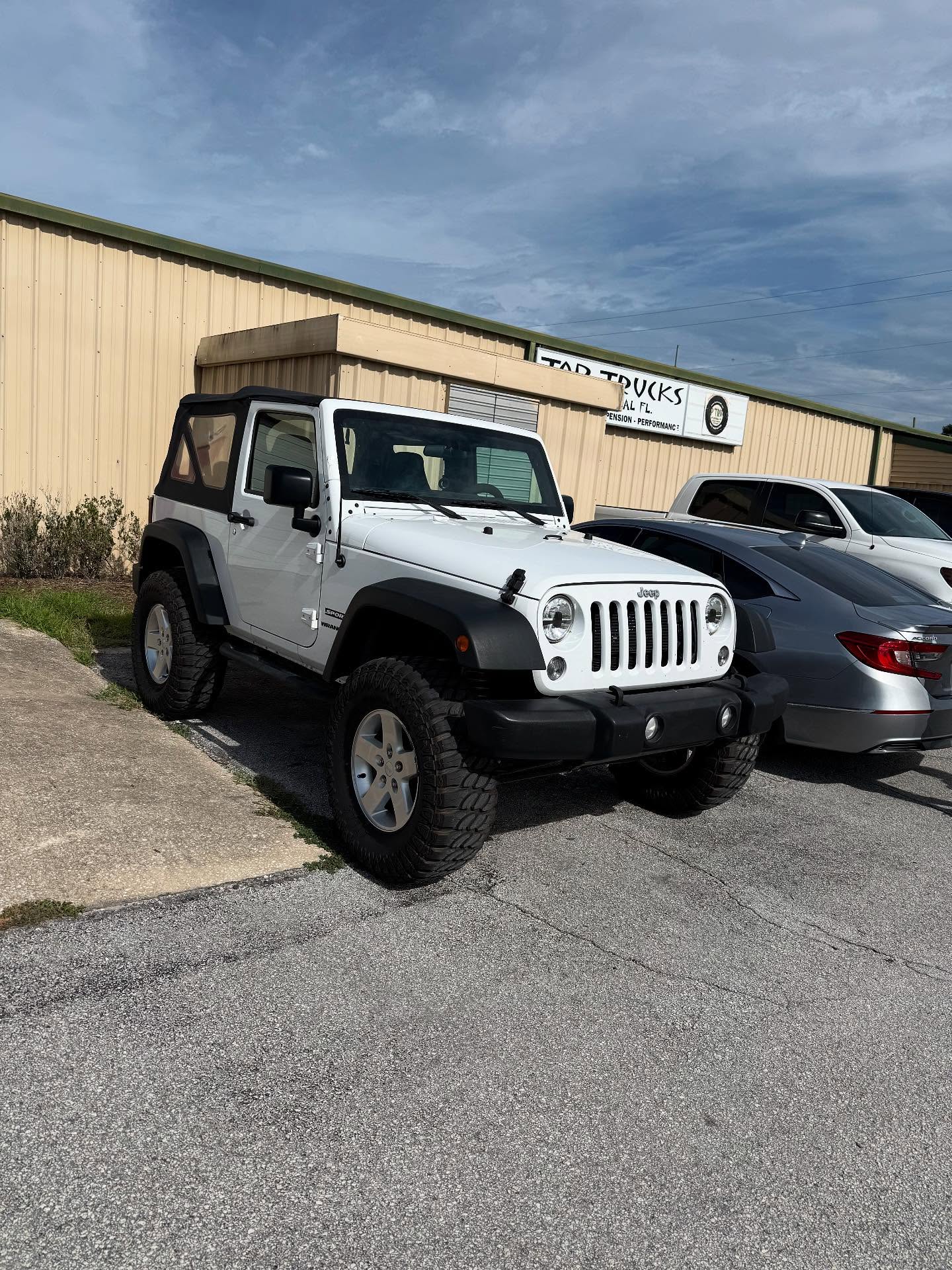 White two-door Jeep Wrangler outside the Top Trucks shop
