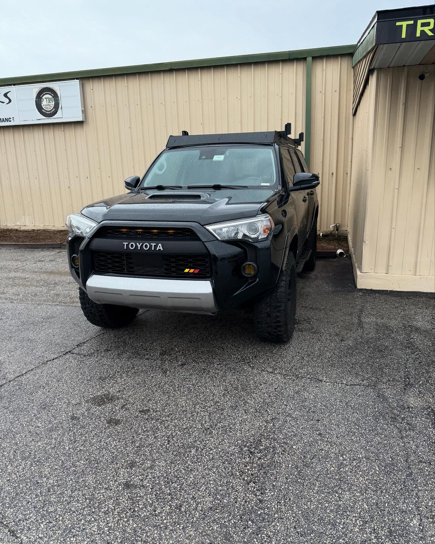 Black Toyota 4Runner with a roof rack outside the Top Trucks shop