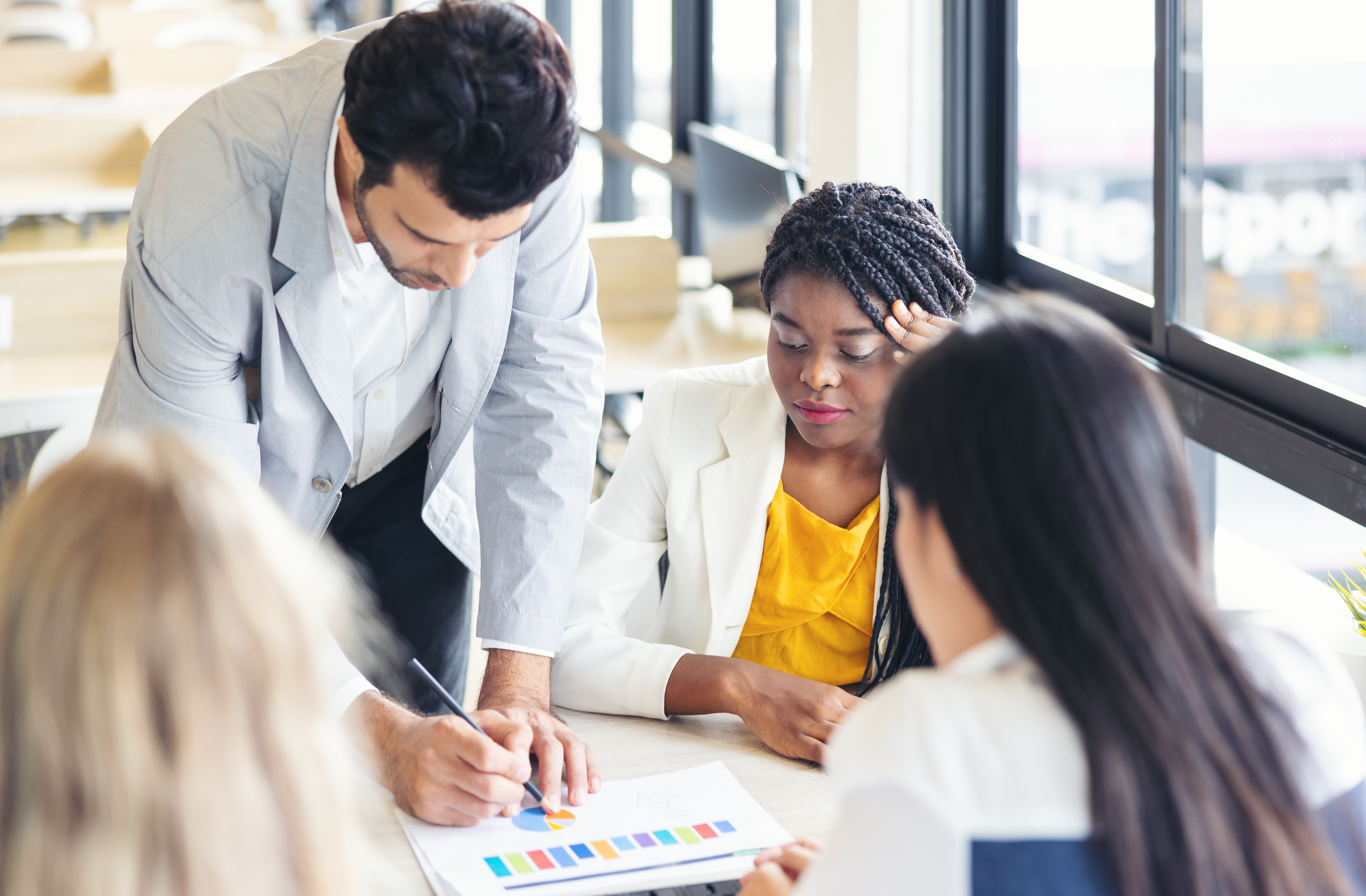 A capable professional sits with a hand to her head as a colleague leans over a chart, the cost of a carried seat landing on the person who keeps absorbing it