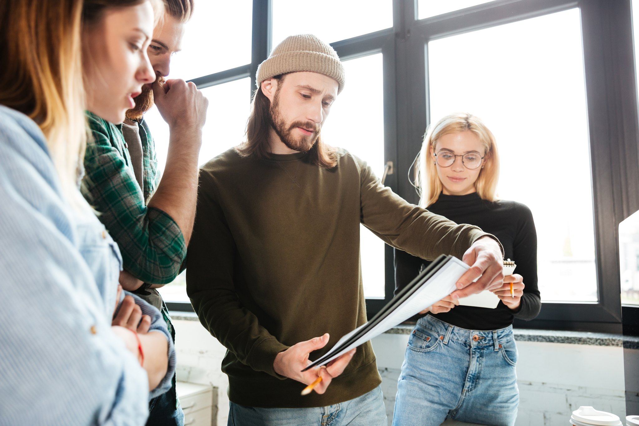 A team stands together problem-solving over a document in natural light, leaning in, the picture of a group where every person is part of it