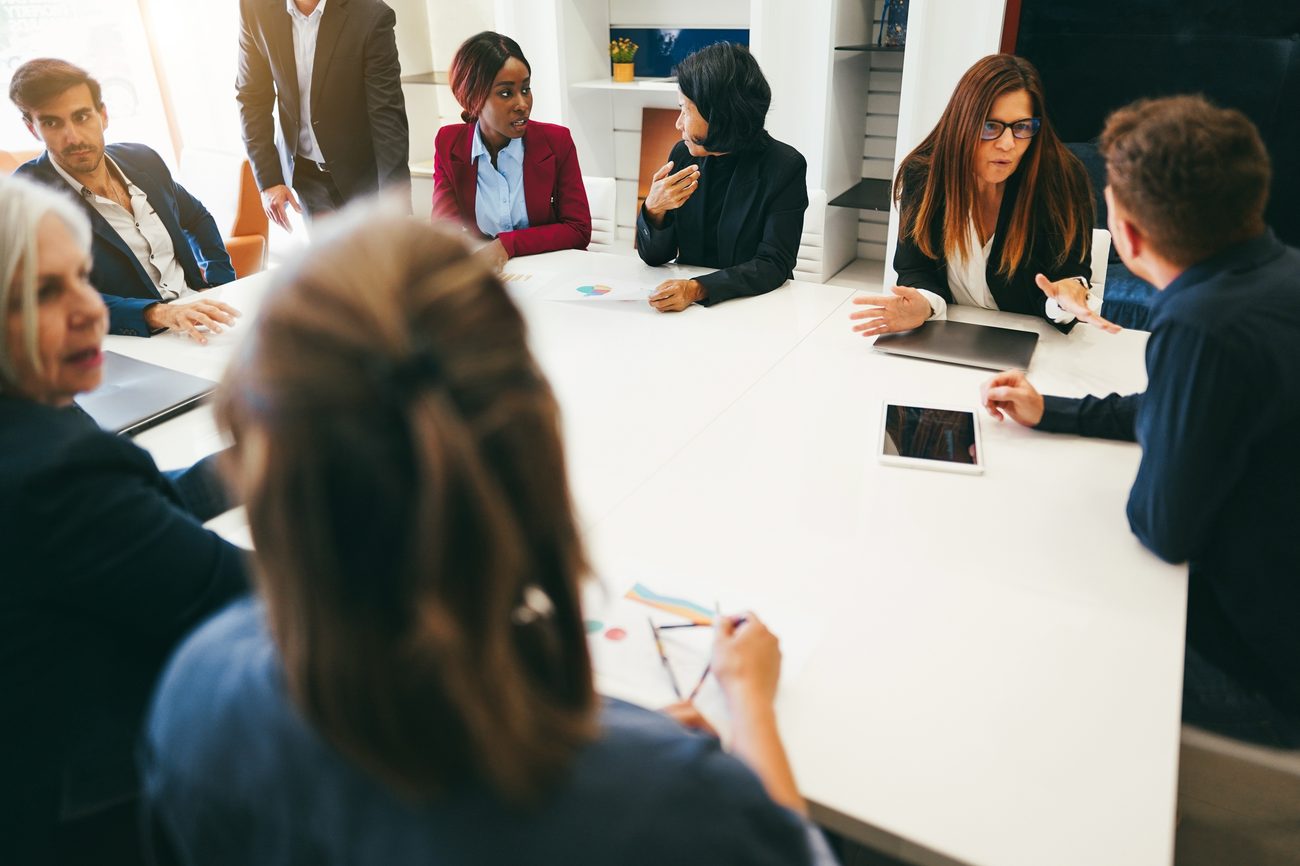 Colleagues around a meeting table seen from a seat at the table, the moment after a question, IEXDG leadership culture