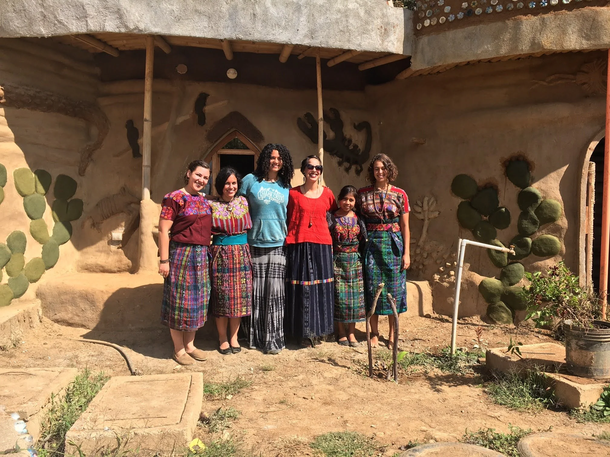 A group of women are doing ecotourism in Guatemala while in front of a clay house dressed in traditional clothing