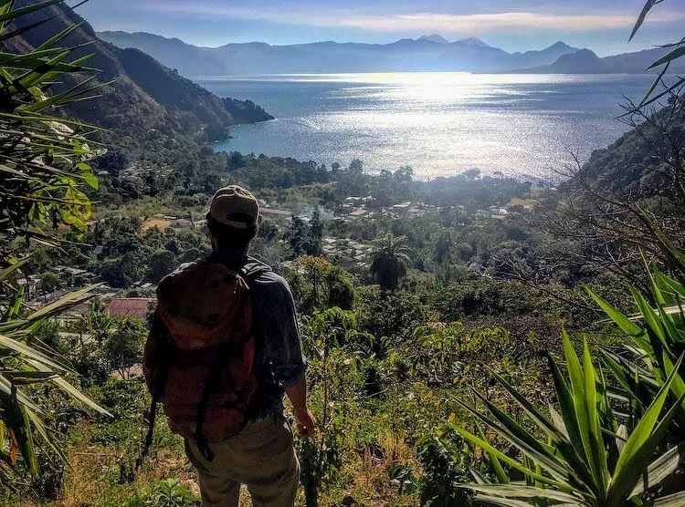 A man in on a hike overlooking the lake and mountains as part of ecotourism in Guatemala