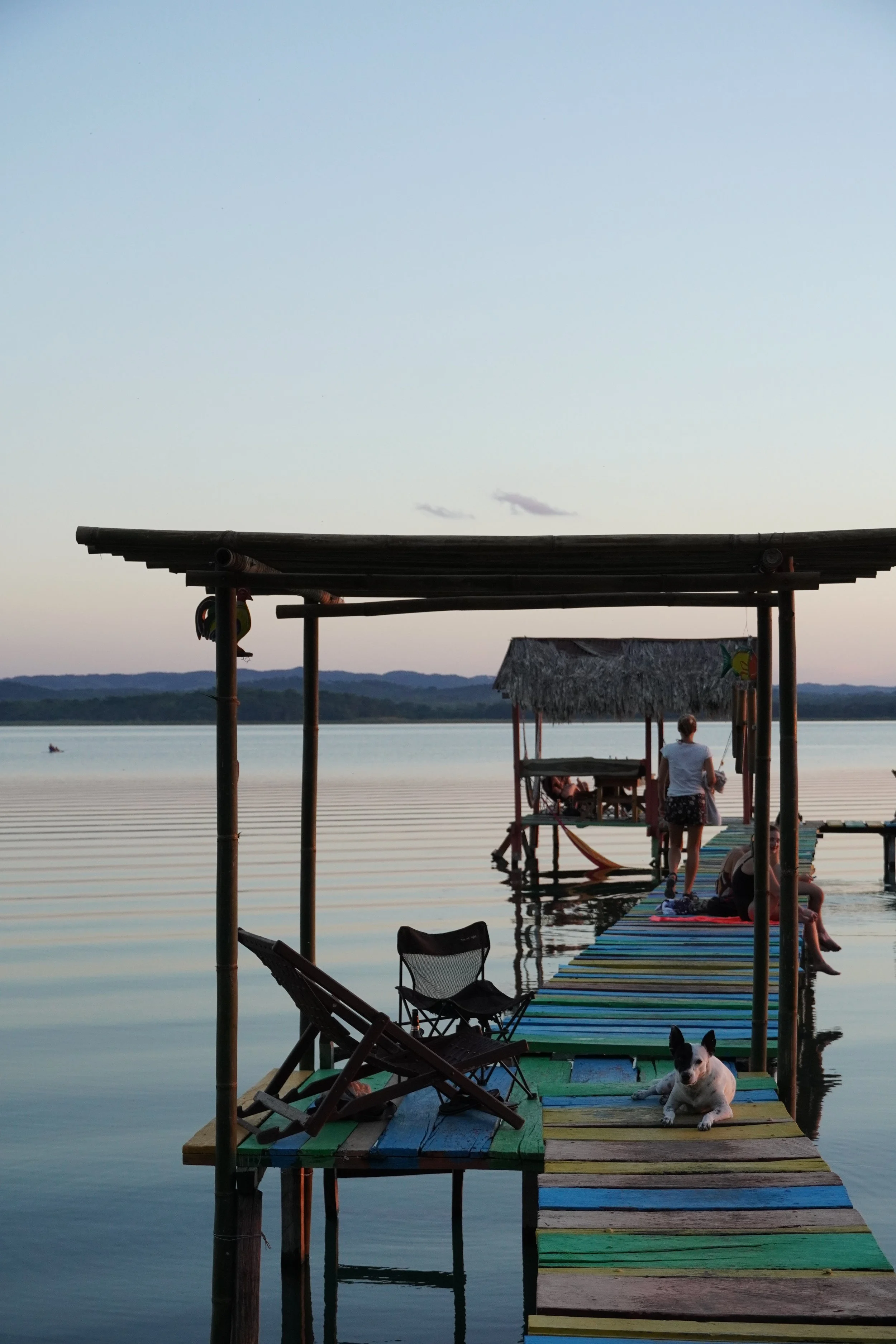A dog and a woman are on a colorful dock on the the Lake at dusk in El Remata, in Peten Guatemala