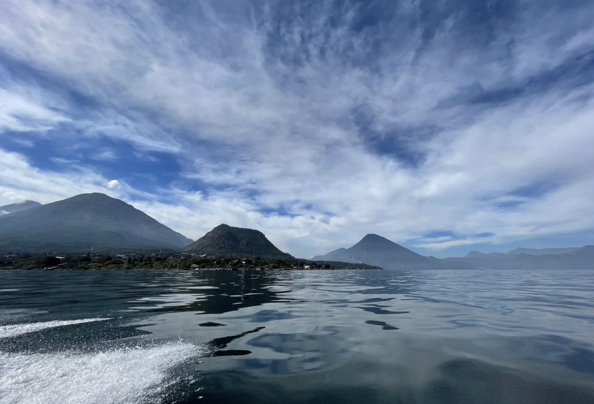 A beautiful photo of Lake Atitlan in Guatemala with blue waters, blue skies, and volcanos in the background.