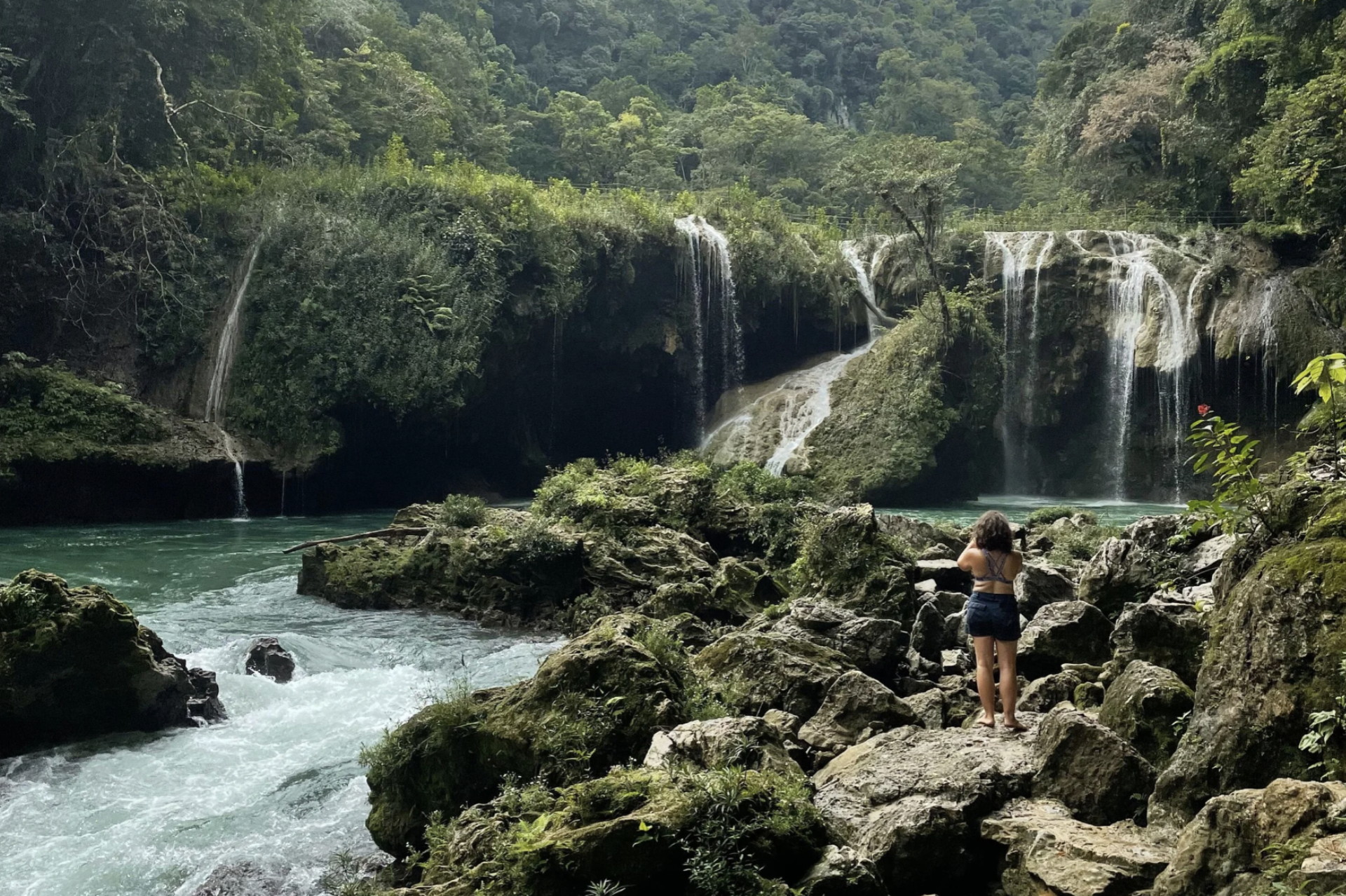 A woman is standing on rocks taking photos of the beautiful waterfalls at Semuc Champey in Guatemala.