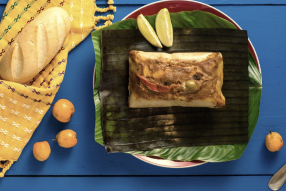 A tamale is on a banana leaf on a plate with fruit, showcasing Guatemalan street food