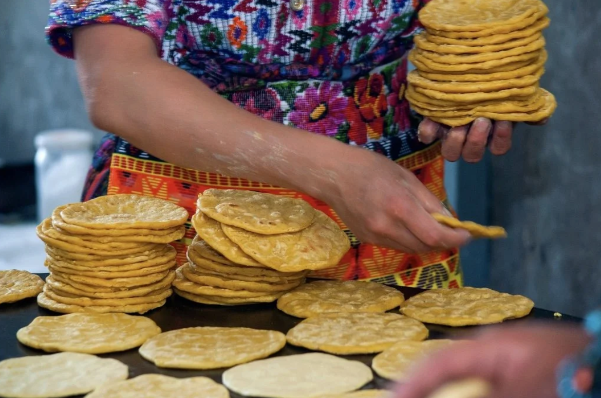 A Guatemalan woman in traditional clothing is hand warming tortillas on a grill, making Guatemalan street food