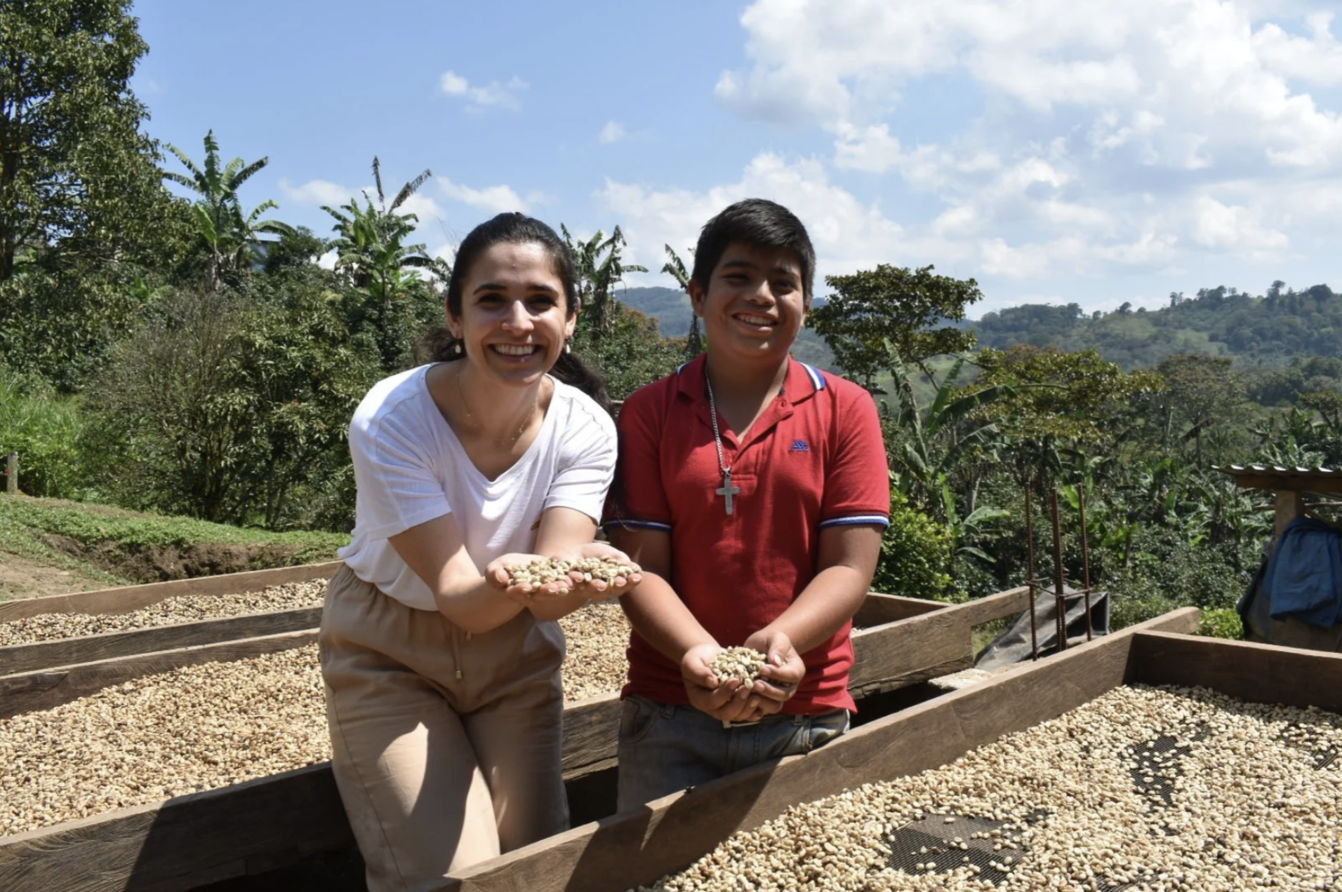 A woman and a boy are holding up coffee beans from the drying racks on a farm international student tours