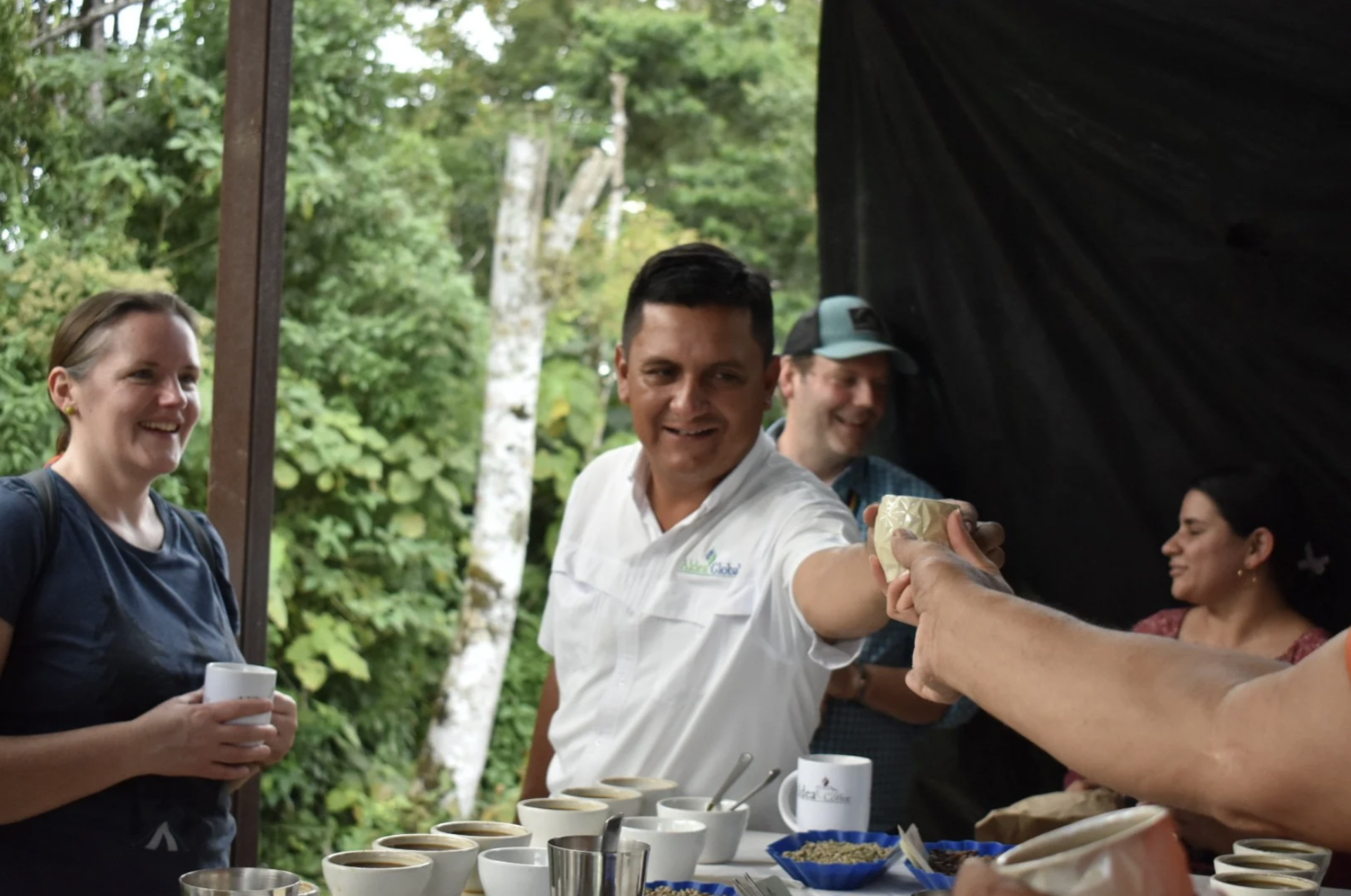 The tour guide is handing a cup of coffee to a student at a group tour on a farm in Nicaragua.