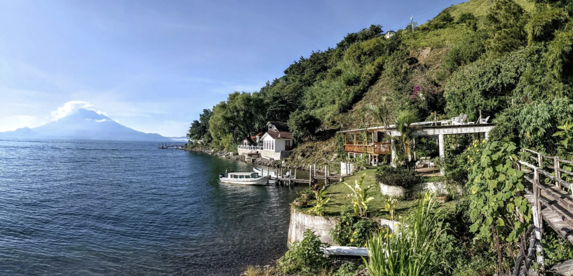 Lake Atitlan on a sunny day with boats and the hillside with a volcano in the background