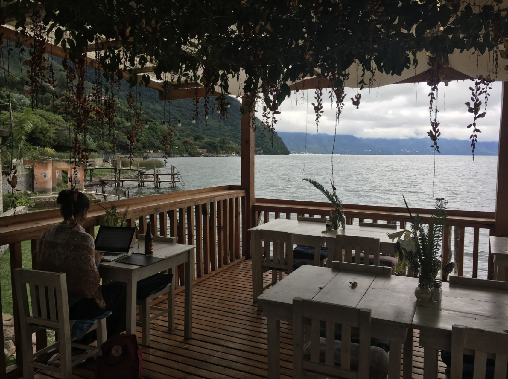 A young woman is working remotely on an outdoor deck overlooking a lake during the seasons of Guatemala
