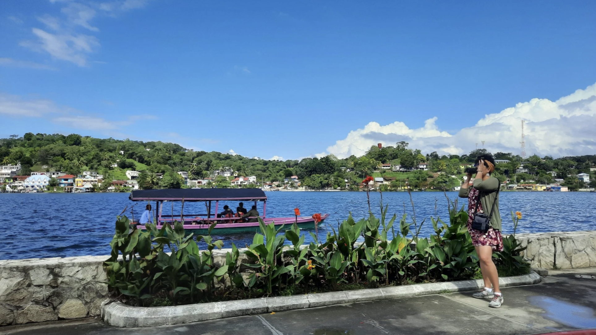 Leilani taking a photo next to Lake Atitlan while a boat cruises by during the warm seasons of Guatemala
