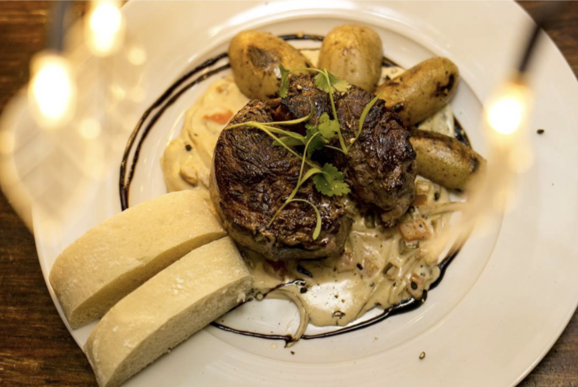A dinner plate showcases creamy pasta underneath grilled meat with a side of potatoes and bread at one of the best restaurants in Antigua Guatemala