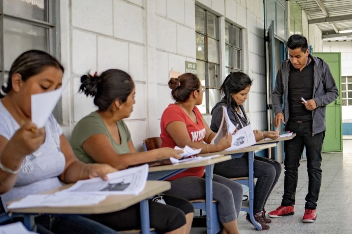 A man is overseeing as a group of women are reviewing materials at the Creamos non profit organization you can donate to on Giving Tuesday