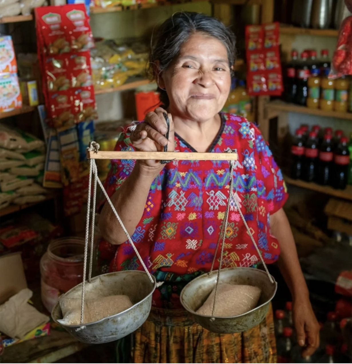 An Indigenous woman is in her shop holding a scale with products in each basket with WCCN, which you can donate to for Giving Tuesday