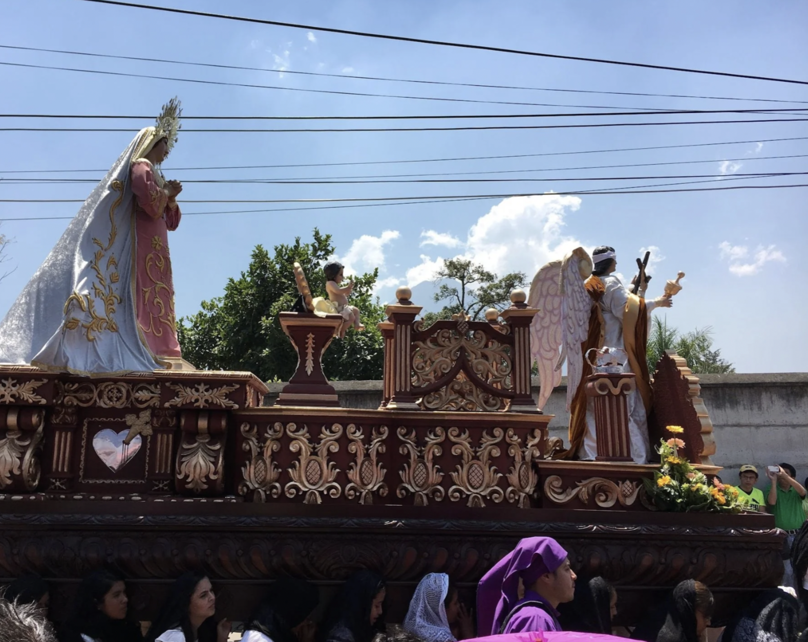 A float is being carried through the streets of Guatemala with angels, baby Jesus, and mother Mary